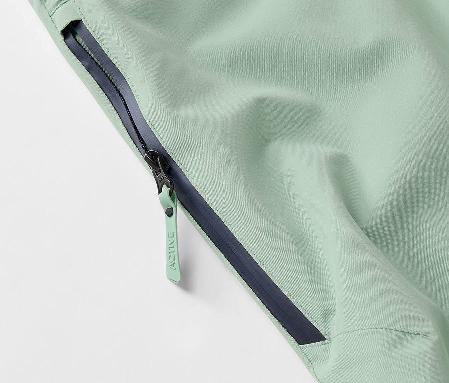 Détail d'une veste vert clair avec une fermeture éclair et un ourlet bleu foncé.