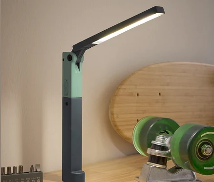 Une lampe de travail LED, un tournevis, un jeu d'embouts et des accessoires de skateboard sont posés sur une table en bois.
