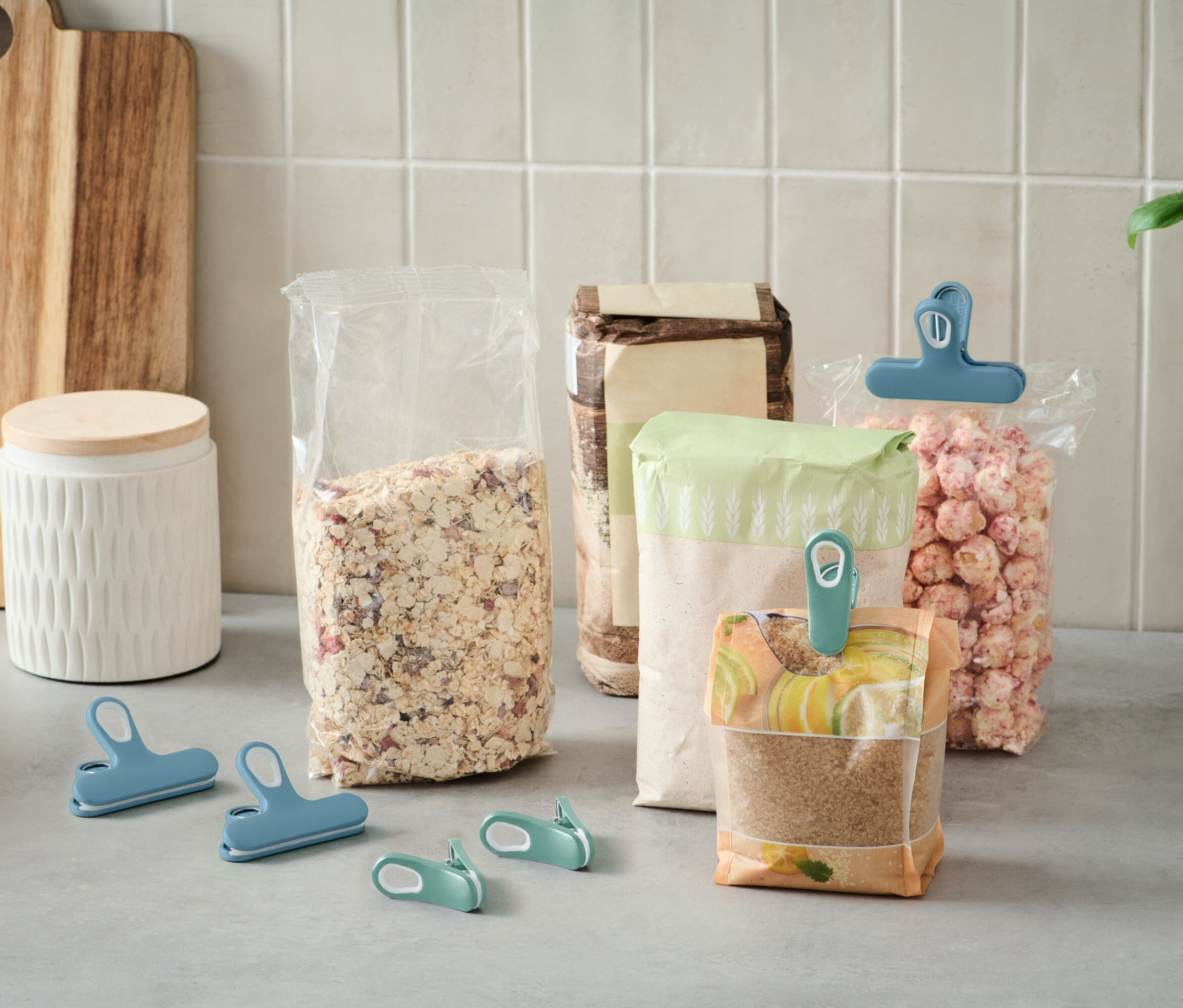 Plusieurs sacs de nourriture ouverts sont posés sur un comptoir de cuisine et sont fermés par des clips colorés.