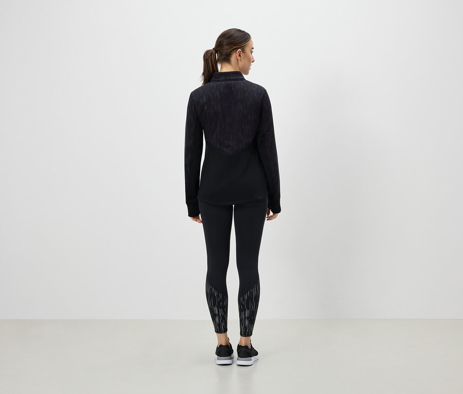 Une femme se tient dos à la caméra et porte des vêtements de sport noirs.