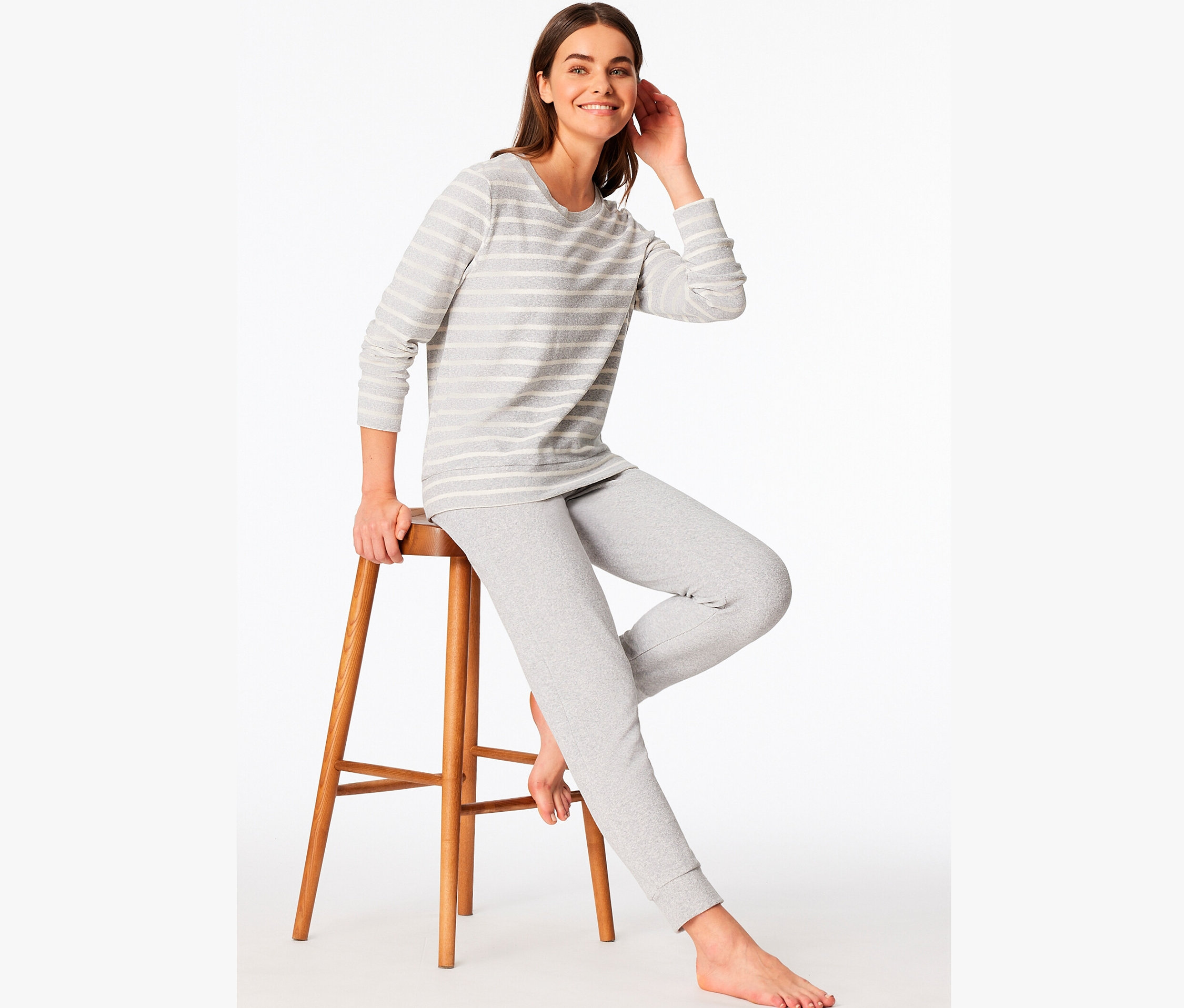 Une femme est assise sur un tabouret en bois et porte un pyjama gris rayé.