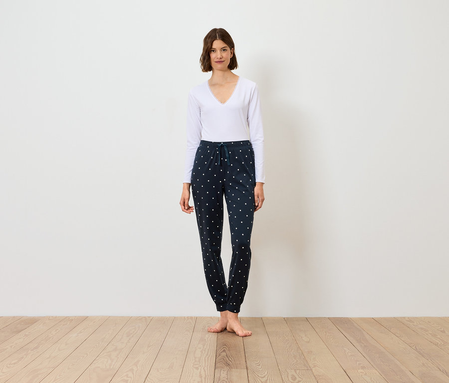 Une femme se tient debout et porte un T-shirt blanc à manches longues et un pantalon bleu marine à motifs.