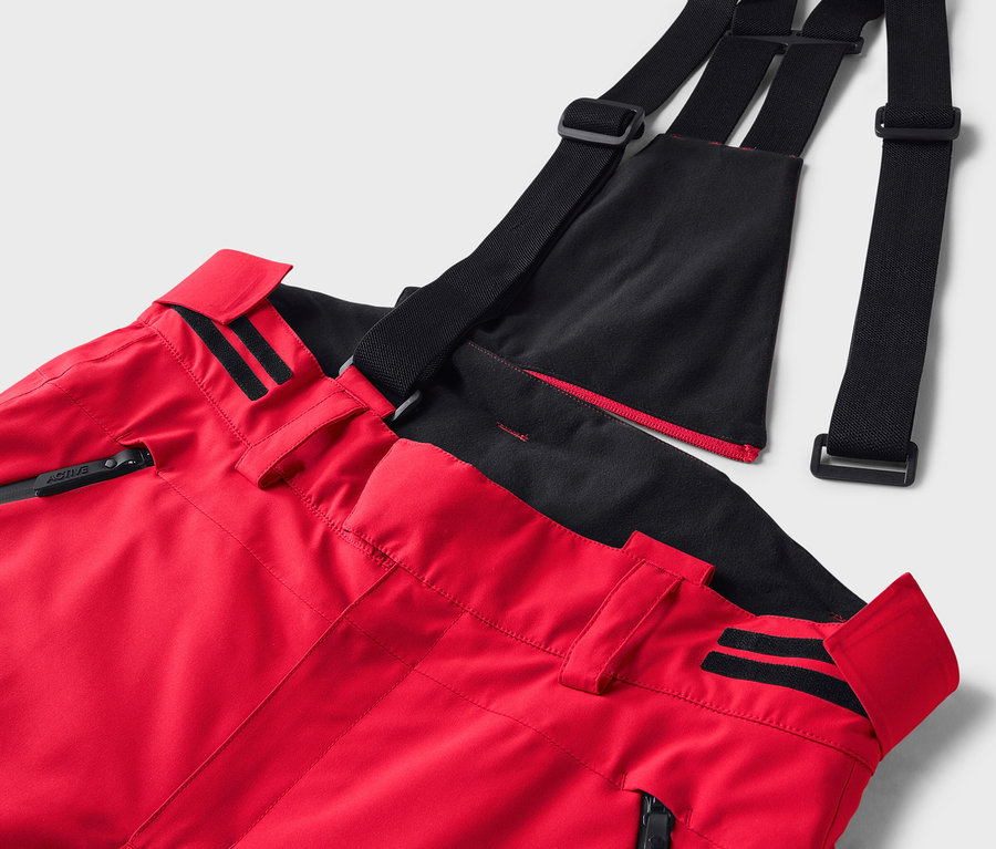 Gros plan sur un pantalon de ski rouge avec des bretelles noires.