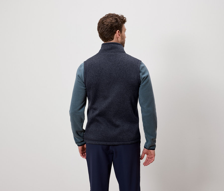 Un homme, vu de dos, porte un gilet bleu marine et un pull bleu.