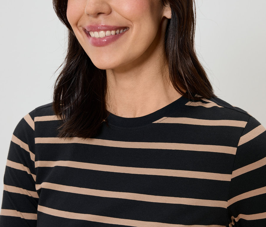 Une femme souriante aux cheveux noirs porte un t-shirt rayé.