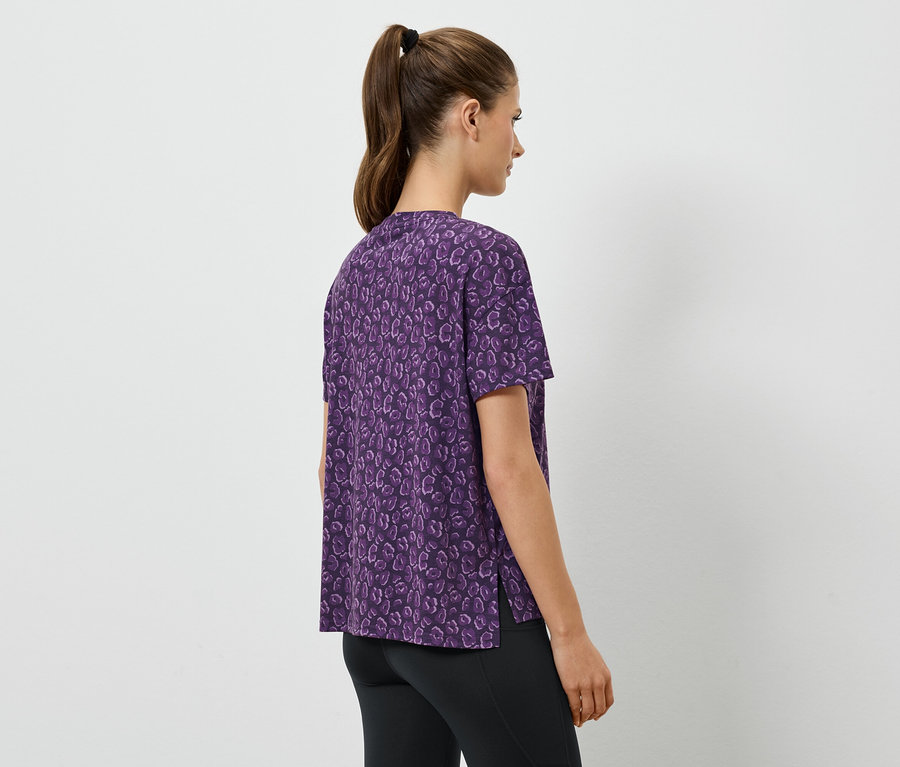 Une femme porte une chemise violette à manches courtes et des leggings noirs.