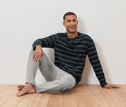 Un homme est assis par terre en pyjama rayé et pantalon gris.