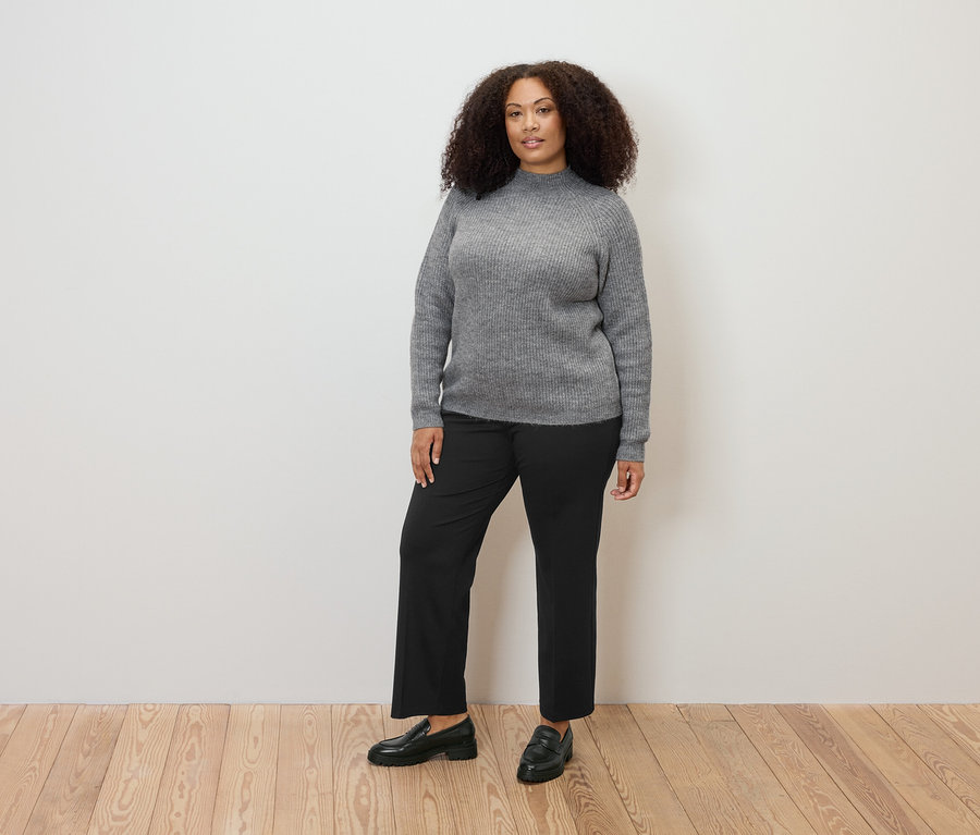 Une femme debout porte un pull à col droit en grosse maille gris et un pantalon en jersey confortable.