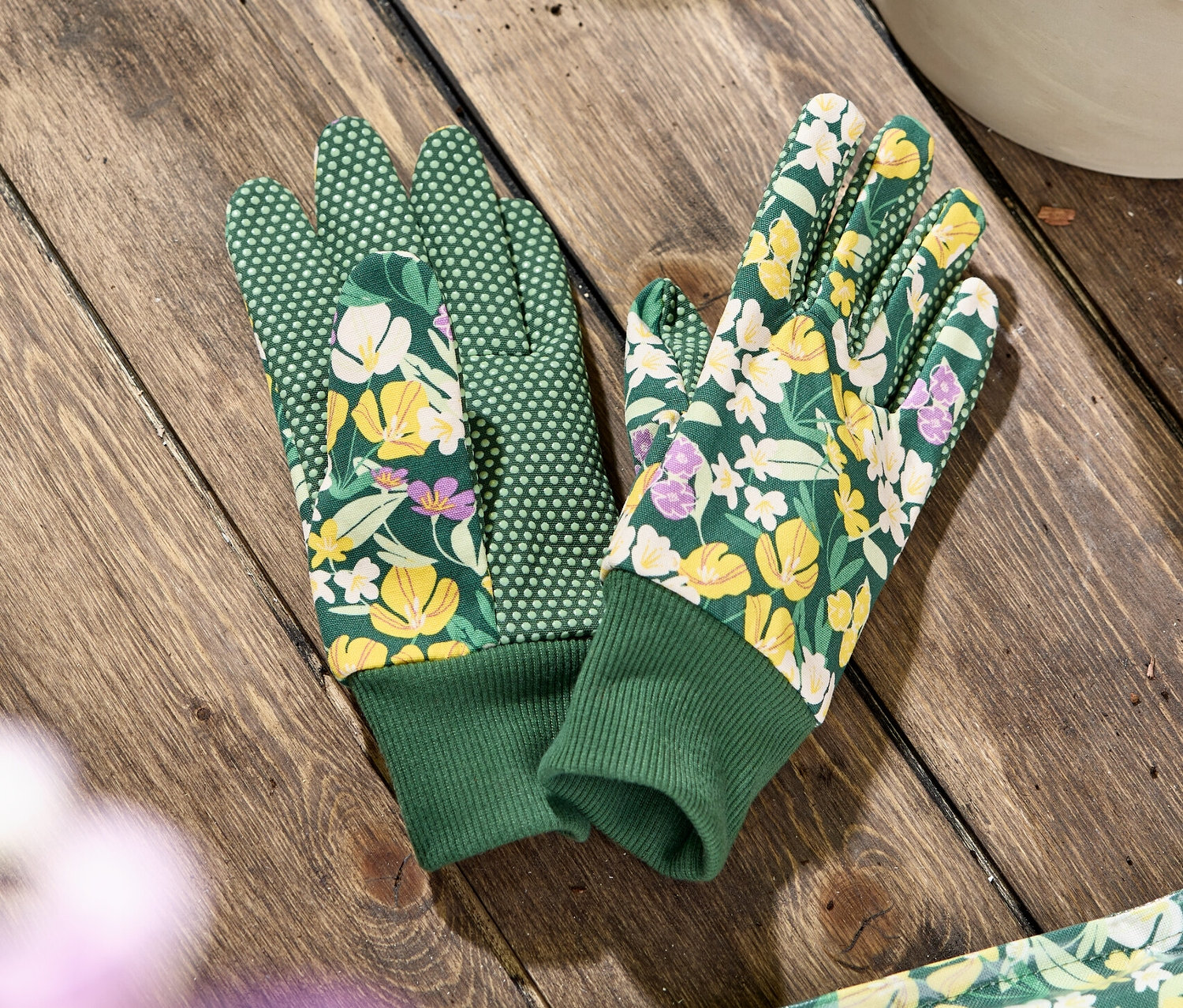 Une paire de gants de jardinage à motif floral est posée sur une table en bois.