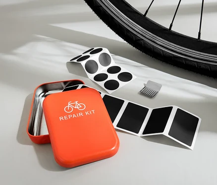 Kit de réparation de vélo orange ouvert avec des patchs et une râpe devant un pneu de vélo.