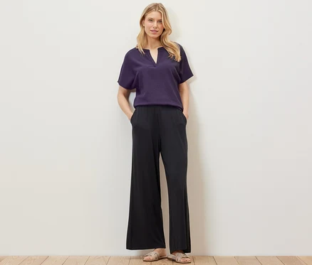 Blonde posant dans un chemisier à manches courtes structuré et un pantalon noir.