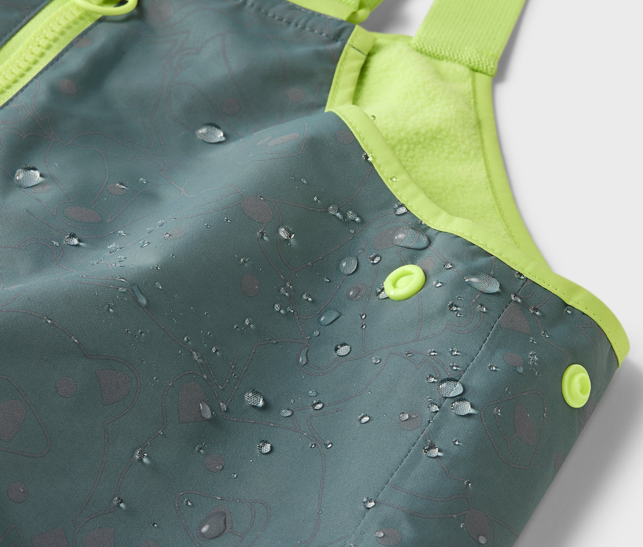Gros plan sur un pantalon de pluie thermique pour enfants avec des éléments réfléchissants et des gouttes d'eau sur la surface.