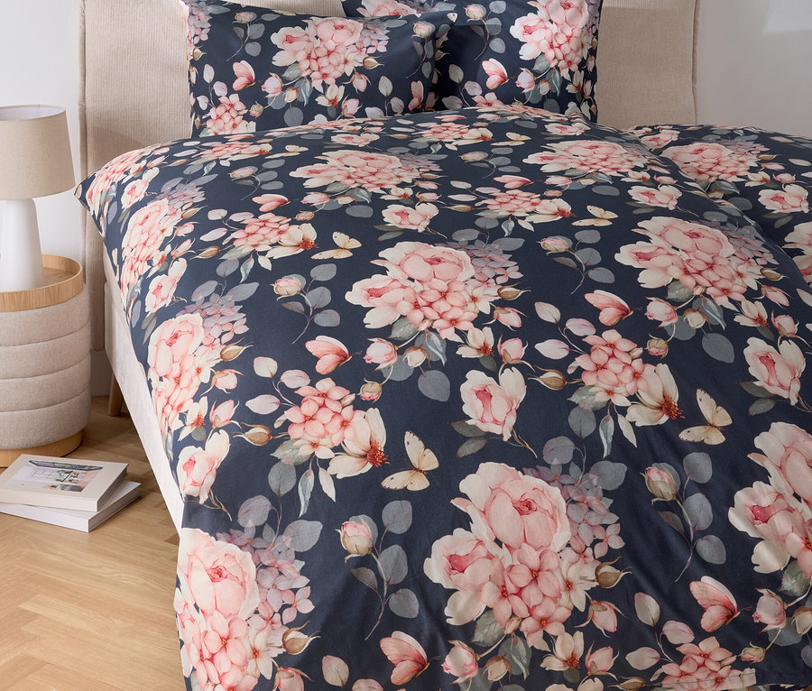 Un lit avec des draps à fleurs et une table de chevet avec une lampe.