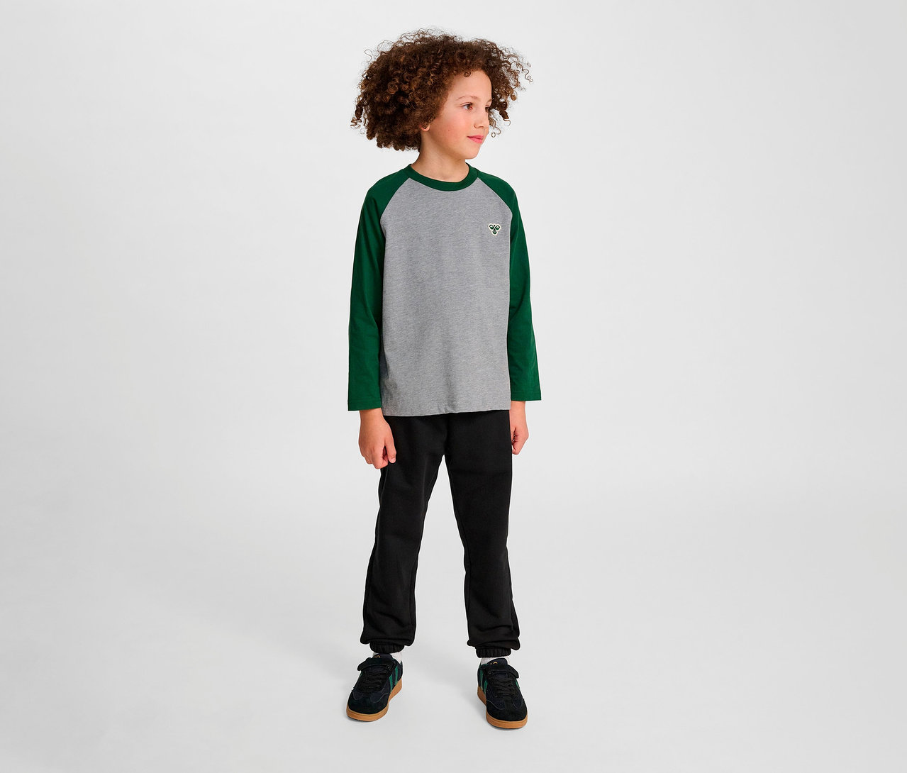 Un garçon debout portant un T-shirt ample à manches raglan HUMMEL HMLJR BEE vert.