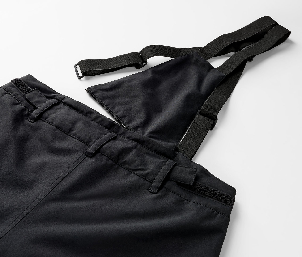 Gros plan d'un pantalon noir à bavette avec des bretelles élastiques.