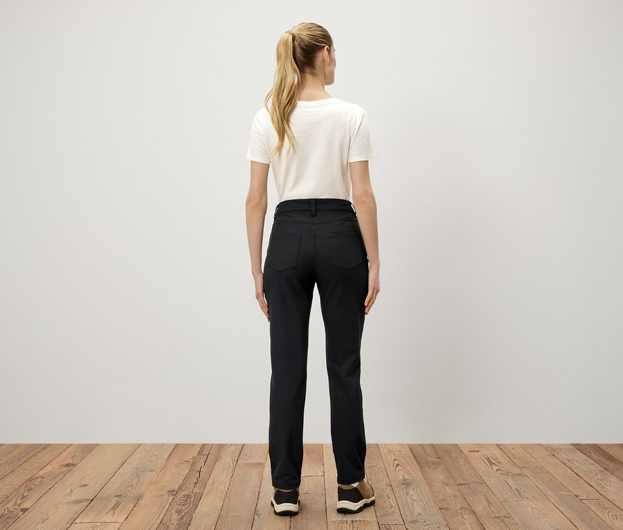 Vue de dos d'une femme aux cheveux blonds attachés en queue de cheval portant un t-shirt blanc et un pantalon noir.