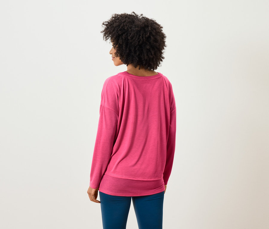 De dos, une femme avec une coiffure afro porte un pull rose et un pantalon bleu.