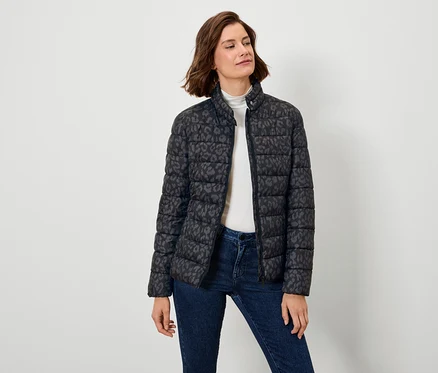 Une femme porte un manteau en duvet noir à motifs et un jean.