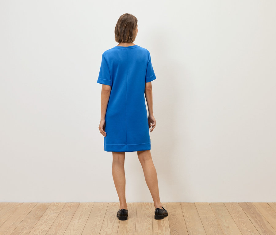 Une femme, vue de dos, porte une robe bleue et des chaussures noires.