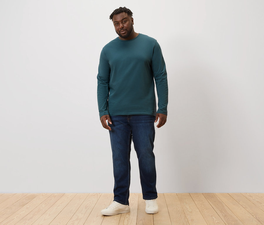 Un homme debout, portant un jean et 2 T-shirts manches longues verts.