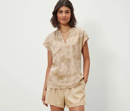Femme portant un chemisier imprimé beige à manches courtes.