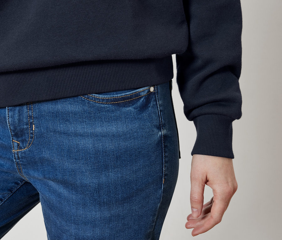 Gros plan d'un jean bleu et d'un pull bleu marine sur le corps d'une personne.