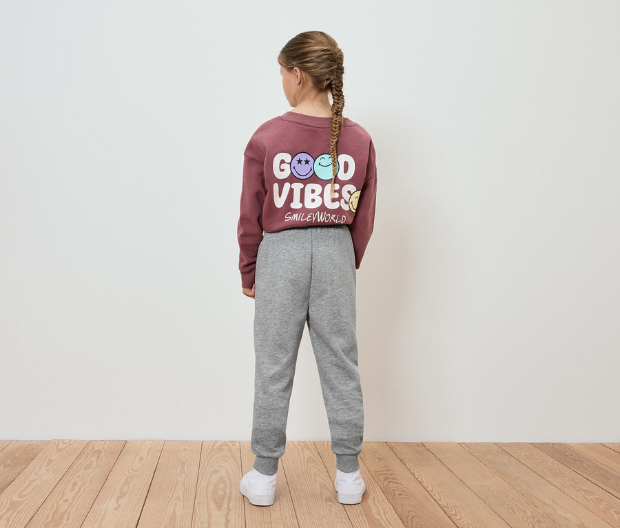 Une fille, vue de dos, porte un sweat-shirt bordeaux avec l'inscription Good Vibes et un jogging gris.