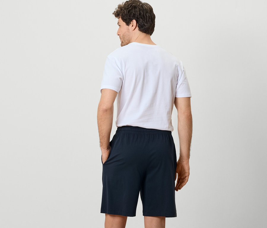 Un homme vu de dos porte 2 shorts de pyjama et un t-shirt.