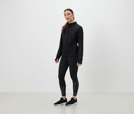 Une femme en tenue de sport noire pose sur un fond clair.