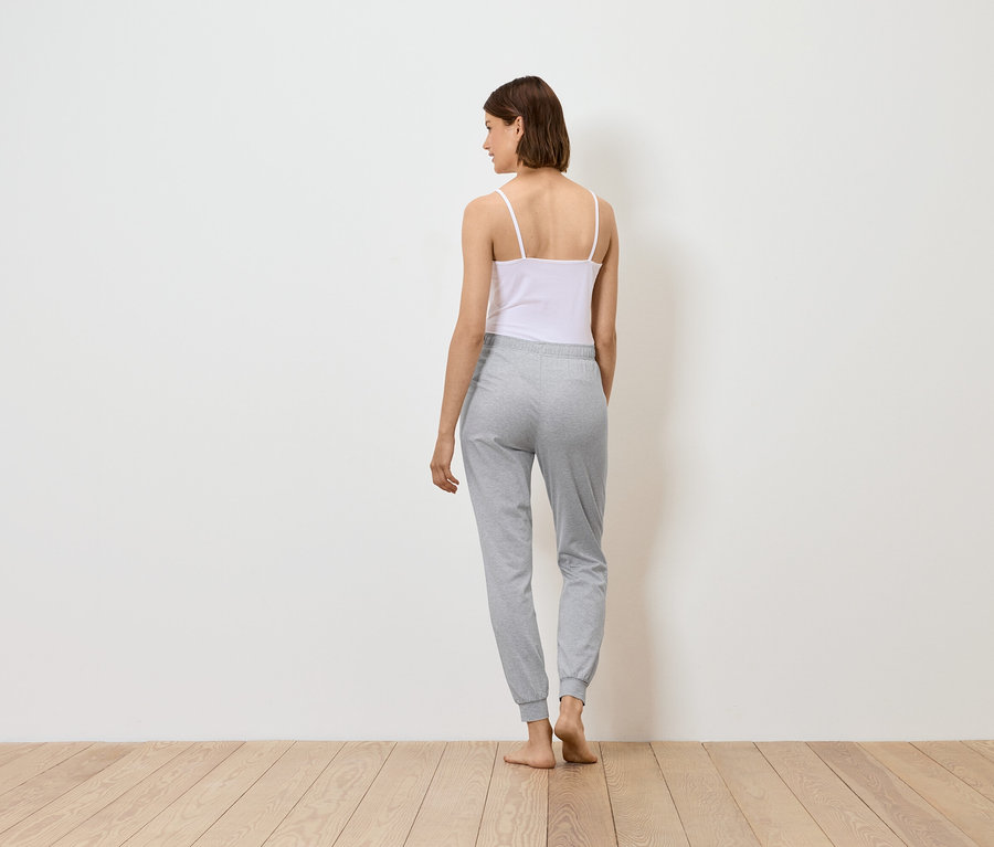 Une femme se tient dos à la caméra, portant un débardeur blanc et un pantalon de survêtement gris.