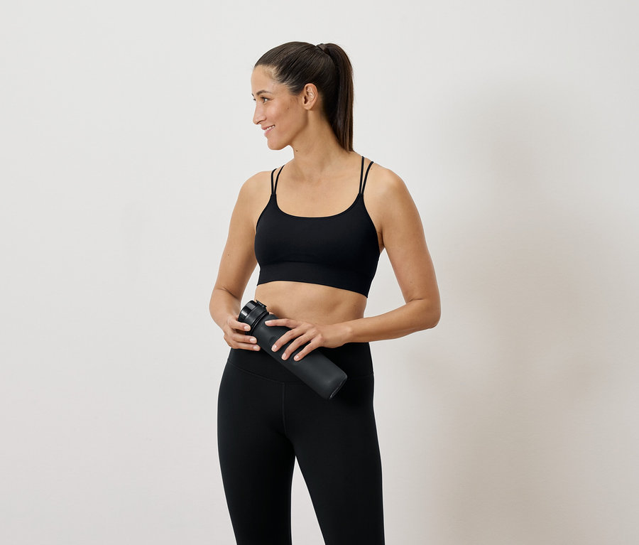 Une femme en tenue de sport noire tient une bouteille d'eau à la main et regarde sur le côté.