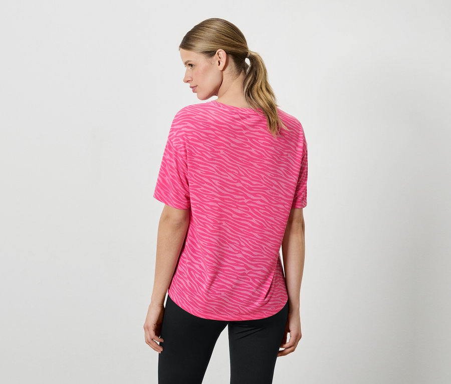 Une femme vue de dos porte un T-shirt rose à motifs animaliers et un pantalon noir.