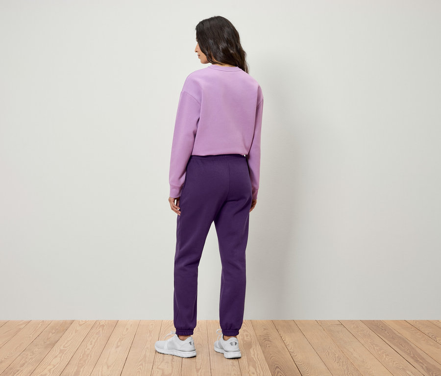 Une femme, vue de dos, porte un sweat-shirt violet et un pantalon de jogging violet.