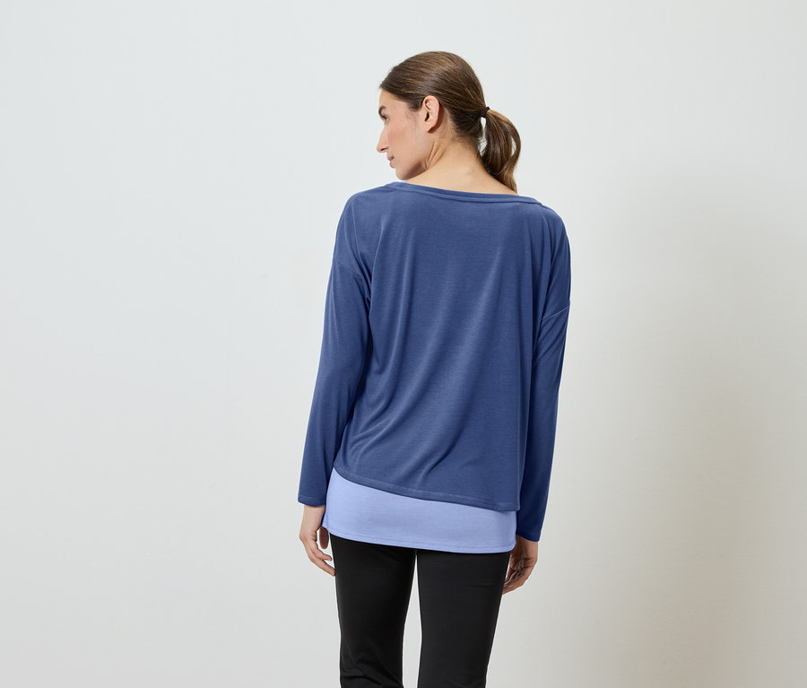 Une femme, dos à la caméra, porte un haut bleu à manches longues et un pantalon noir.