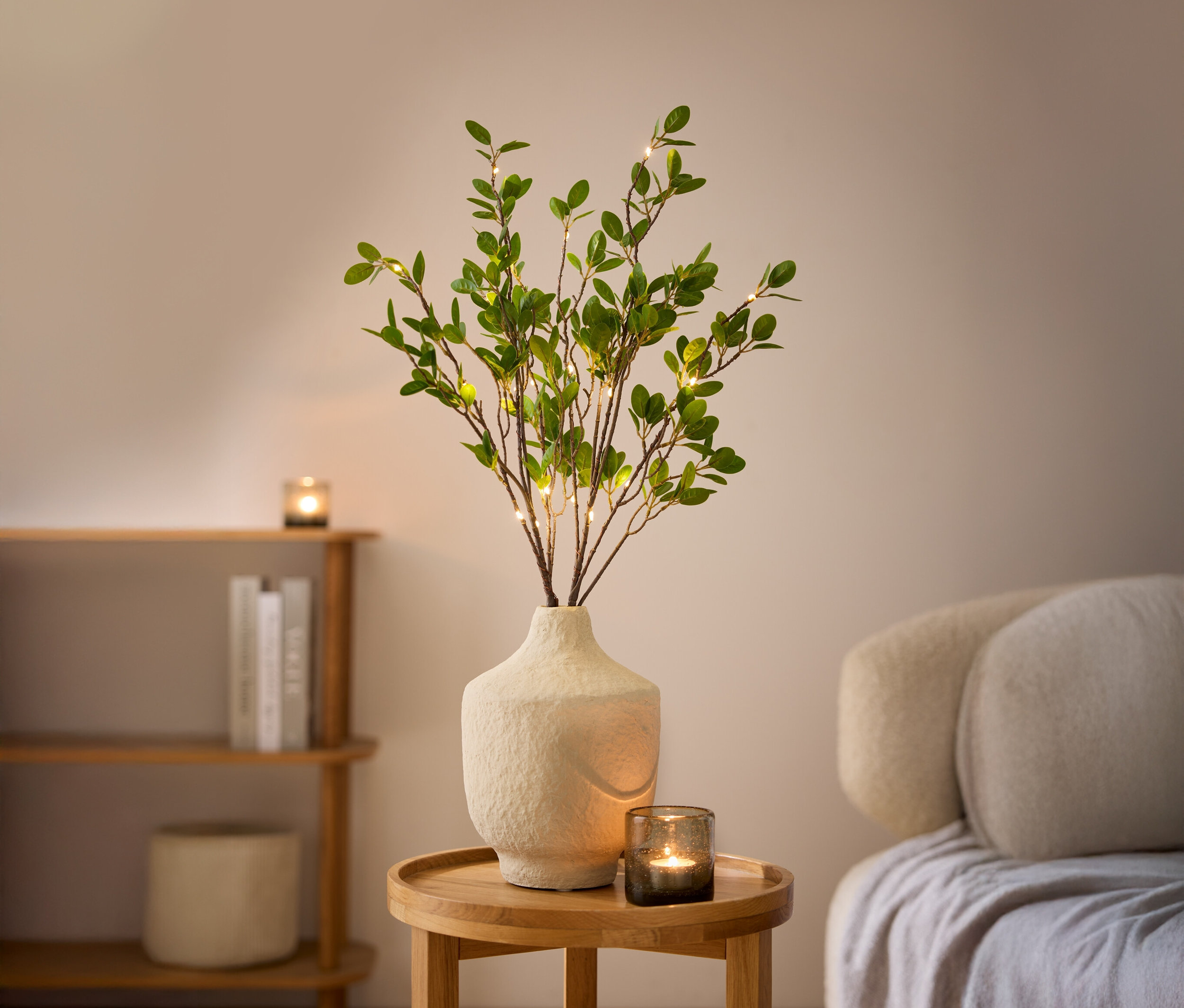 Deux branches décoratives LED dans un vase blanc sur une table en bois.