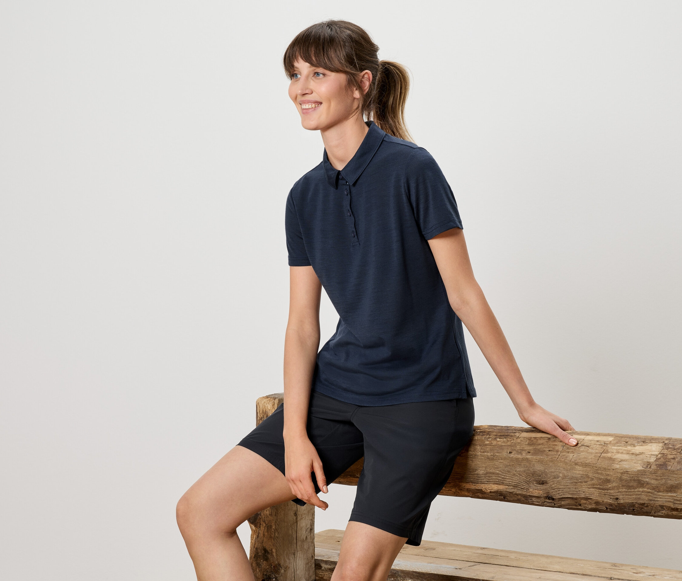 Femme assise sur un banc en bois, portant un polo bleu marine et un short.