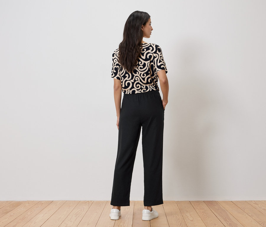 Une femme, vue de dos, porte un chemisier à motifs et un pantalon noir.