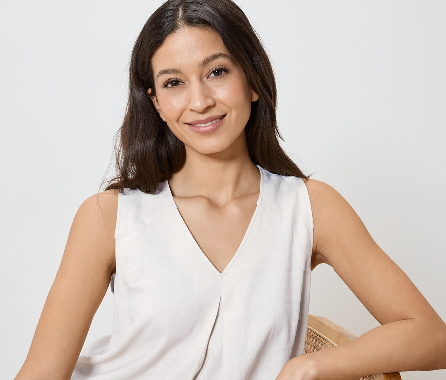 Femme souriante aux cheveux foncés portant un haut clair sans manches à col en V.