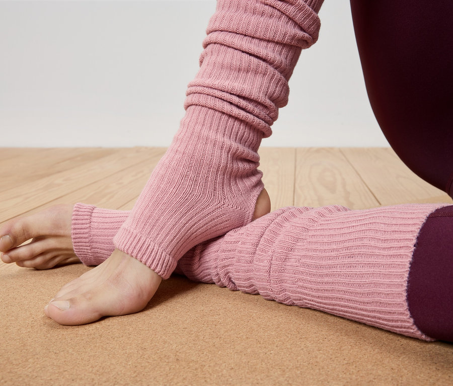 Gros plan d'une personne portant des jambières roses et des leggings bordeaux sur un tapis de yoga marron.