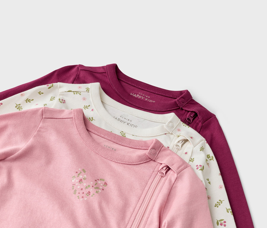 Gros plan sur trois bodies à manches longues pour bébé : rose avec un cœur, blanc avec un motif floral et violet avec une fermeture éclair.