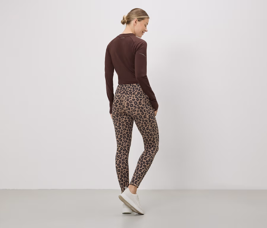 Une femme vue de dos, portant un haut marron, un legging imprimé léopard et des baskets blanches.