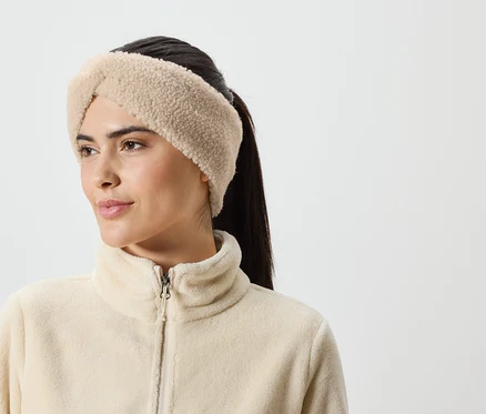 Une femme aux cheveux bruns porte un bandeau beige et une veste en polaire zippée sur un fond blanc.