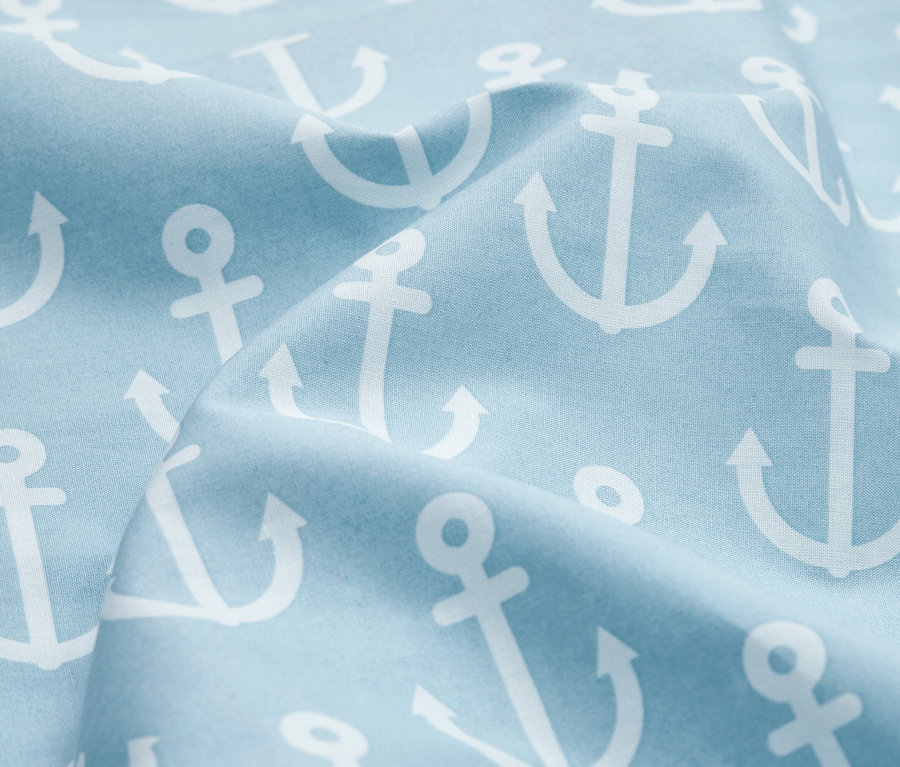Gros plan d'un tissu bleu clair avec des motifs d'ancres blanches et des plis.