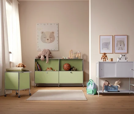 Une chambre d'enfant avec des armoires de rangement vert clair et blanches, des jouets et des photos au mur.