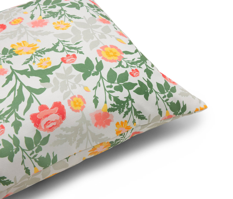 Gros plan d'un coussin à motifs floraux dans les tons rouge, jaune et vert sur fond blanc.