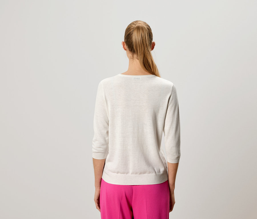 Vue de dos d'une femme aux cheveux blonds portant un pull clair et un pantalon rose.