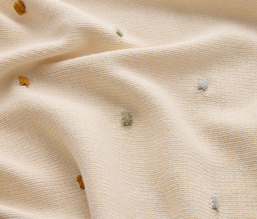 Gros plan d'un tricot crème avec des picots jaunes, verts et gris.