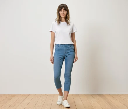 Femme en t-shirt blanc et jean bleu debout devant un mur.