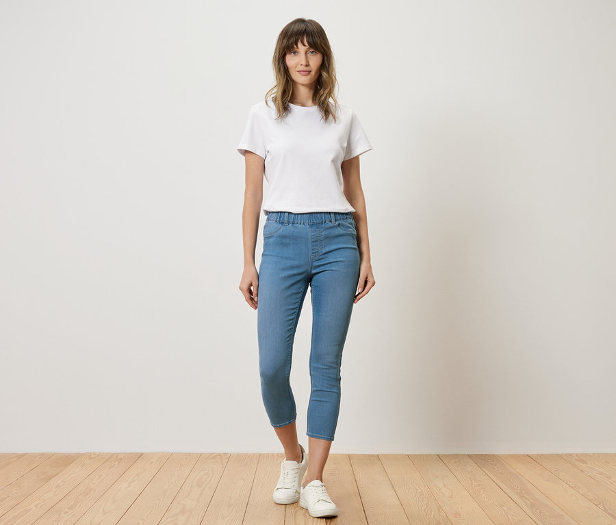 Femme en t-shirt blanc et jean bleu debout devant un mur.