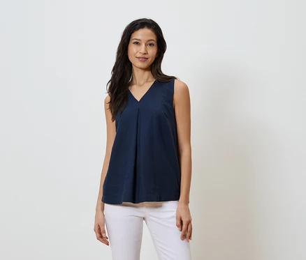 Une femme porte un haut bleu marine sans manches à col en V et un jean blanc.
